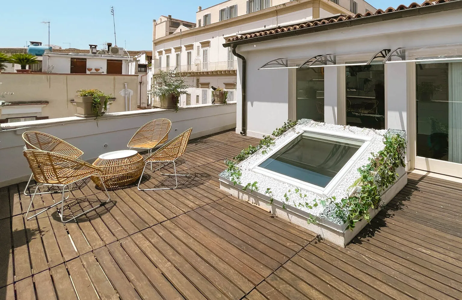 Il terrazzino della suite con poltroncine in vimini e tavolino rotondo sulla pedana in legno, affacciato sui tetti del centro