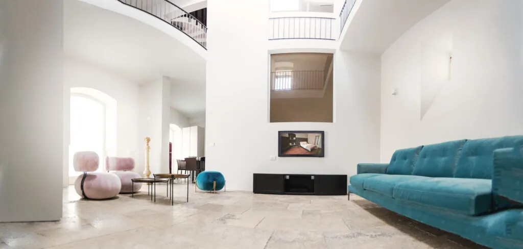 Panoramica della zona living con divano azzurro, pouf rosa e ballatoio