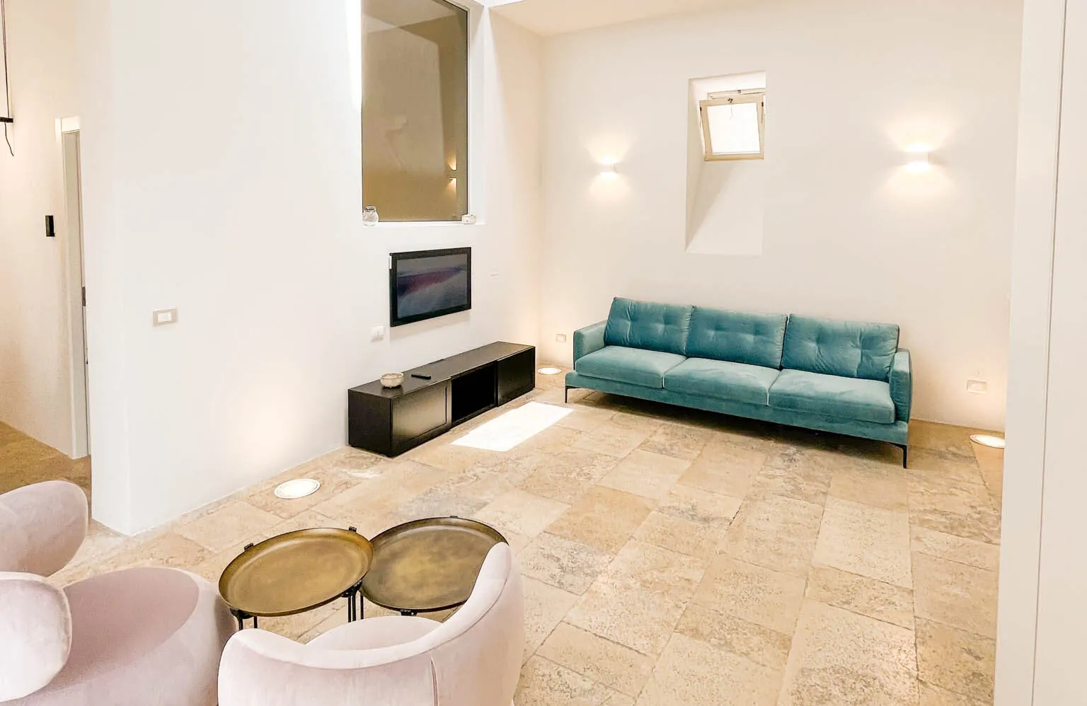 La sala relax con divano azzurro, poltroncine rosa, tavolini in ottone e televisore a parete