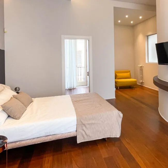 Camera Xylo: letto matrimoniale, parquet scuro, poltrona gialla e porta-finestra sul balcone