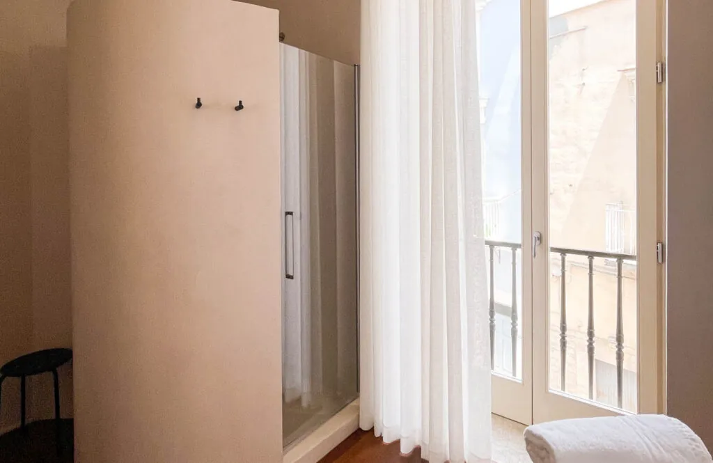 Angolo della camera con doccia in vetro accanto alla porta finestra con tende chiare