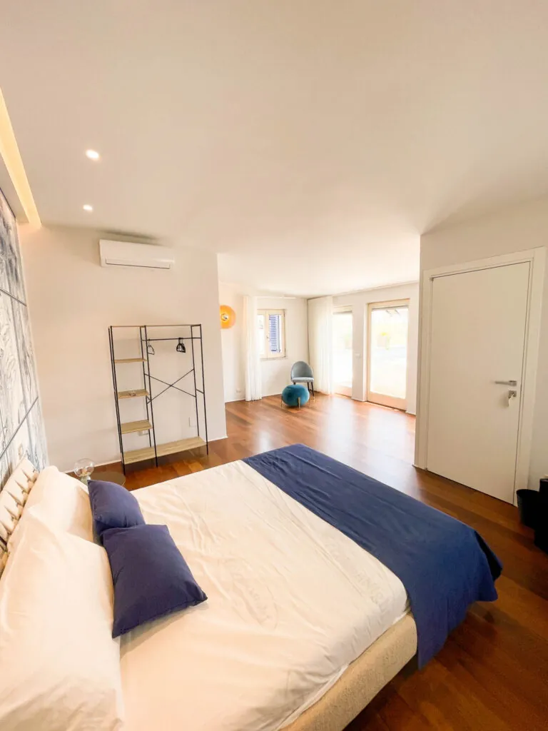 Il letto matrimoniale della camera Fos con cuscini blu e la porta-finestra sul fondo
