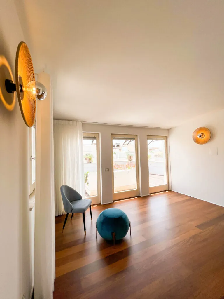 La zona giorno della camera Fos con poltroncina, pouf azzurro e applique a disco