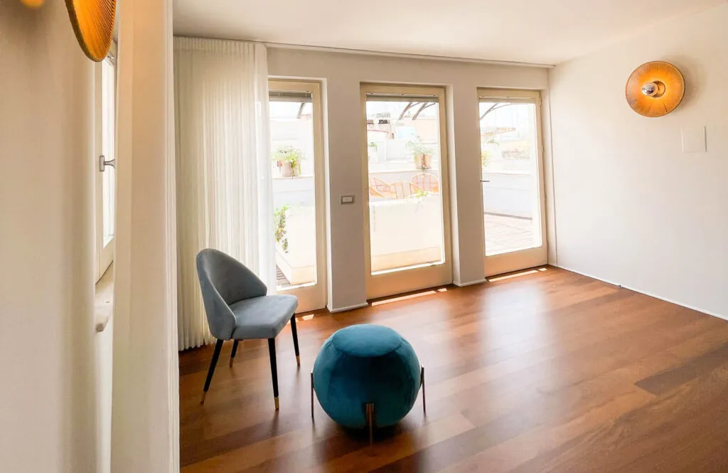 Angolo salotto della camera con poltroncina e pouf verde davanti alle porte finestre