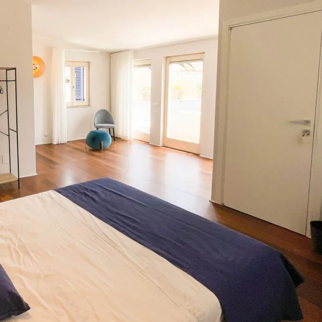 Camera Fos: letto matrimoniale con copriletto blu, parquet e vetrate che si aprono sulla terrazza privata