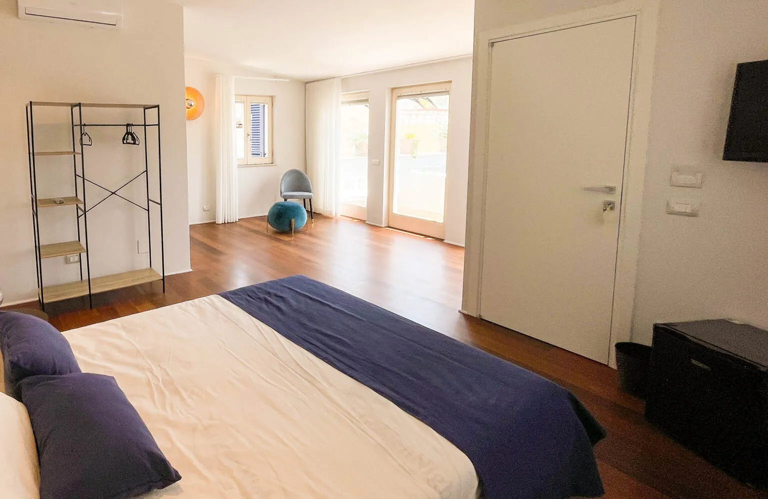 La camera Fos: letto matrimoniale con copriletto blu, pavimento in legno e porta-finestra sulla terrazza