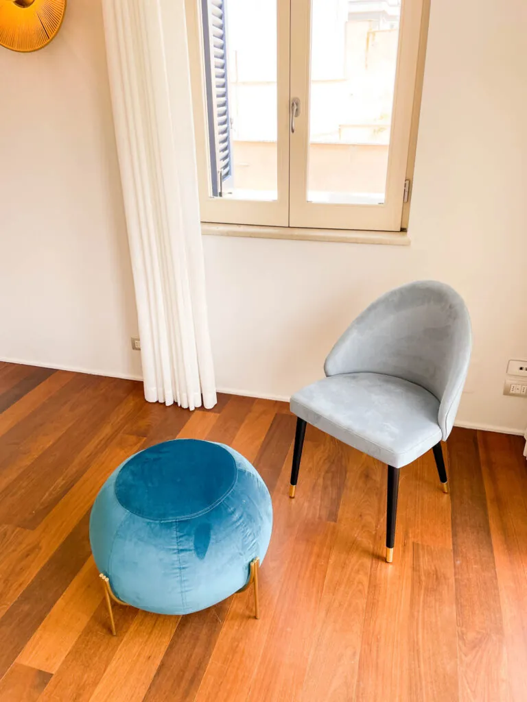 Poltroncina grigia e pouf azzurro davanti alla finestra della camera Fos