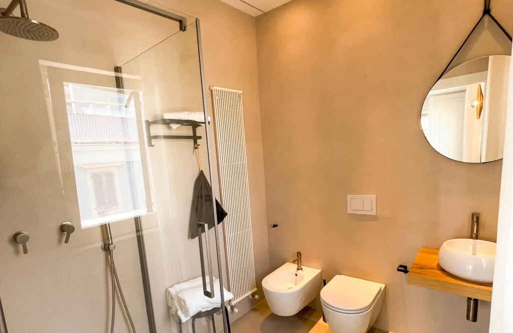 Bagno della camera con doccia in vetro, sanitari sospesi e lavabo d’appoggio su mensola in legno