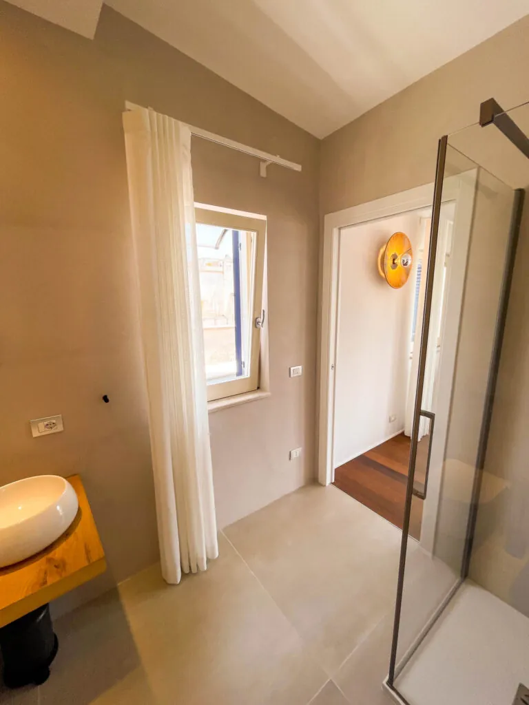 Il bagno della camera Fos con lavabo giallo, tende chiare e box doccia