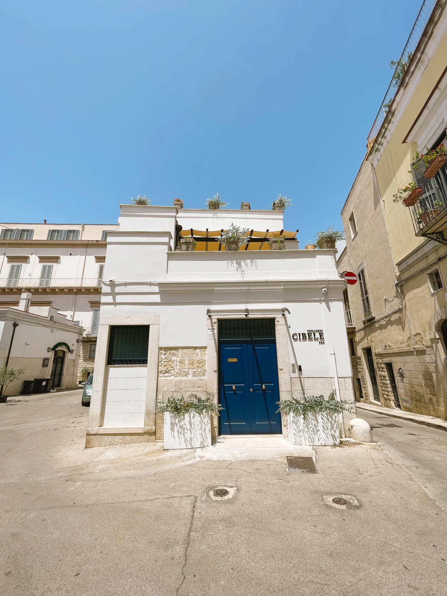 Facciata bianca del B&B Terrazzini Cibele con portone blu, insegna sulla parete e tende gialle sulla terrazza in alto