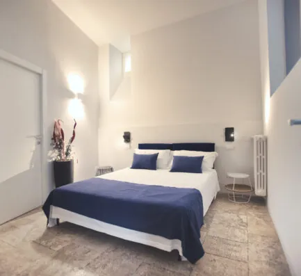 La camera Pètra: letto matrimoniale con copriletto blu e pavimento in pietra chiara