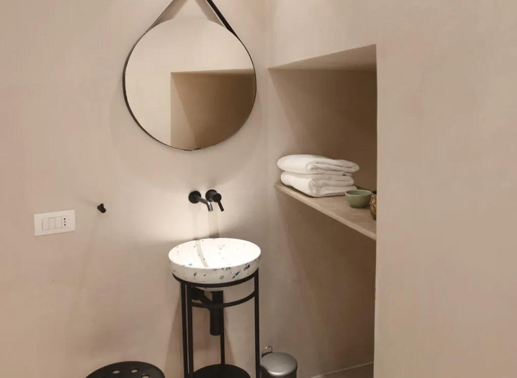 Bagno con specchio tondo, lavabo su struttura in metallo e nicchia con asciugamani