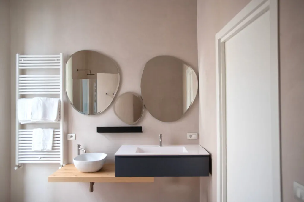 Bagno con due specchi tondi, lavabo su mensola in legno e scaldasalviette